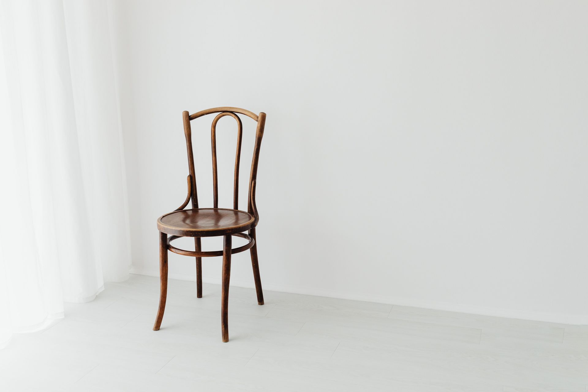 A simple wooden chair sits in a bright, minimalist interior with a white background.